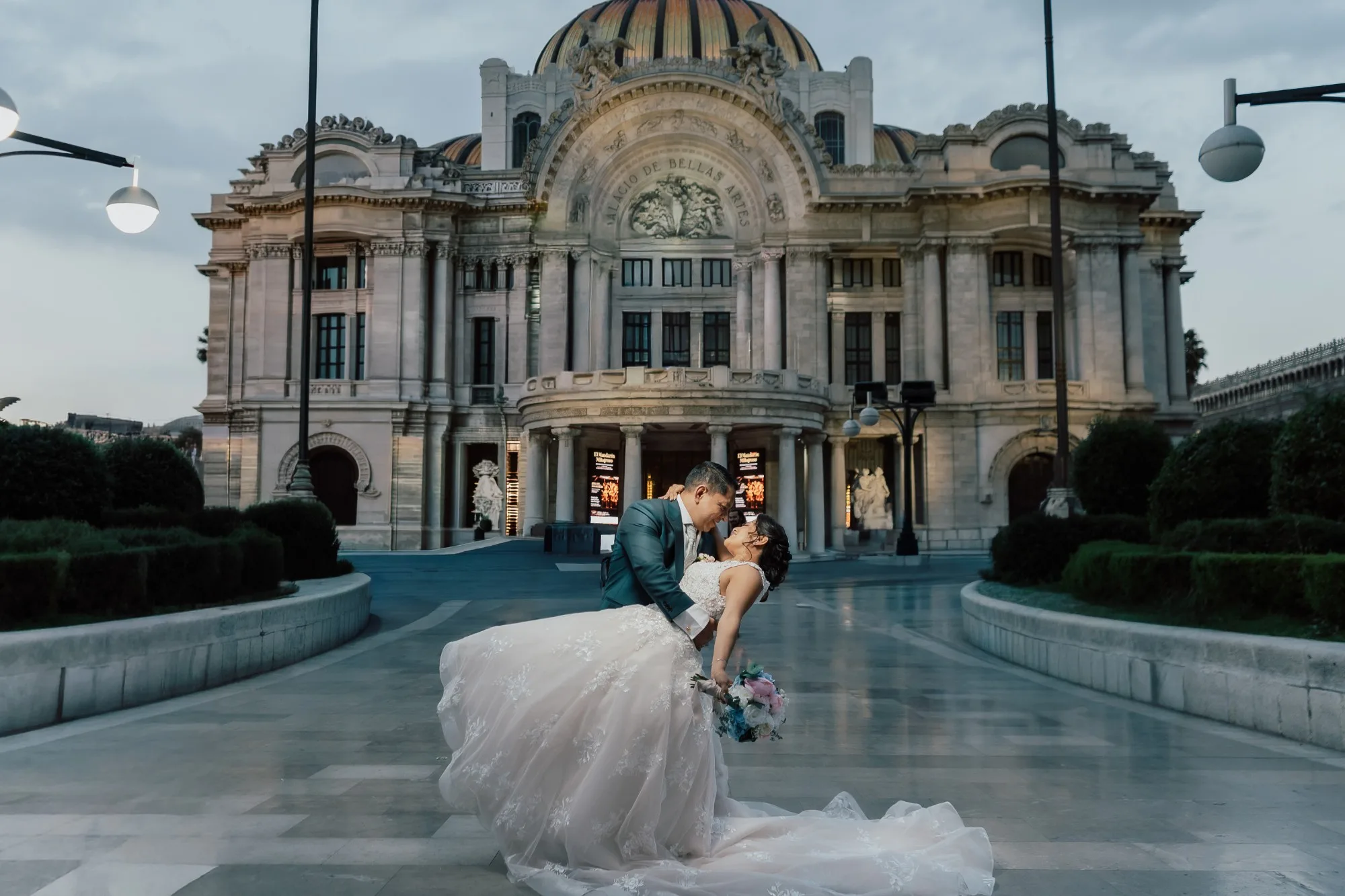 Pareja de recién casados bailando frente al Palacio de Bellas Artes en la Ciudad de México al atardecer.