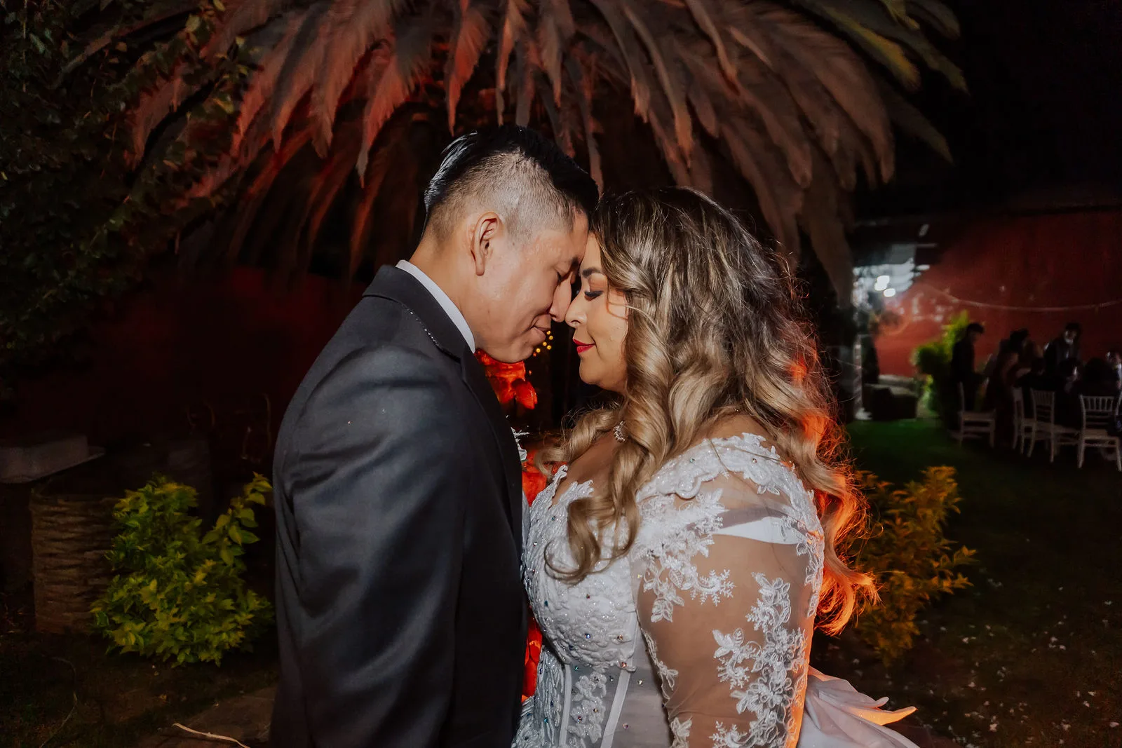 Pareja de recién casados frente con frente en el jardín de su recepción de boda por la noche.
