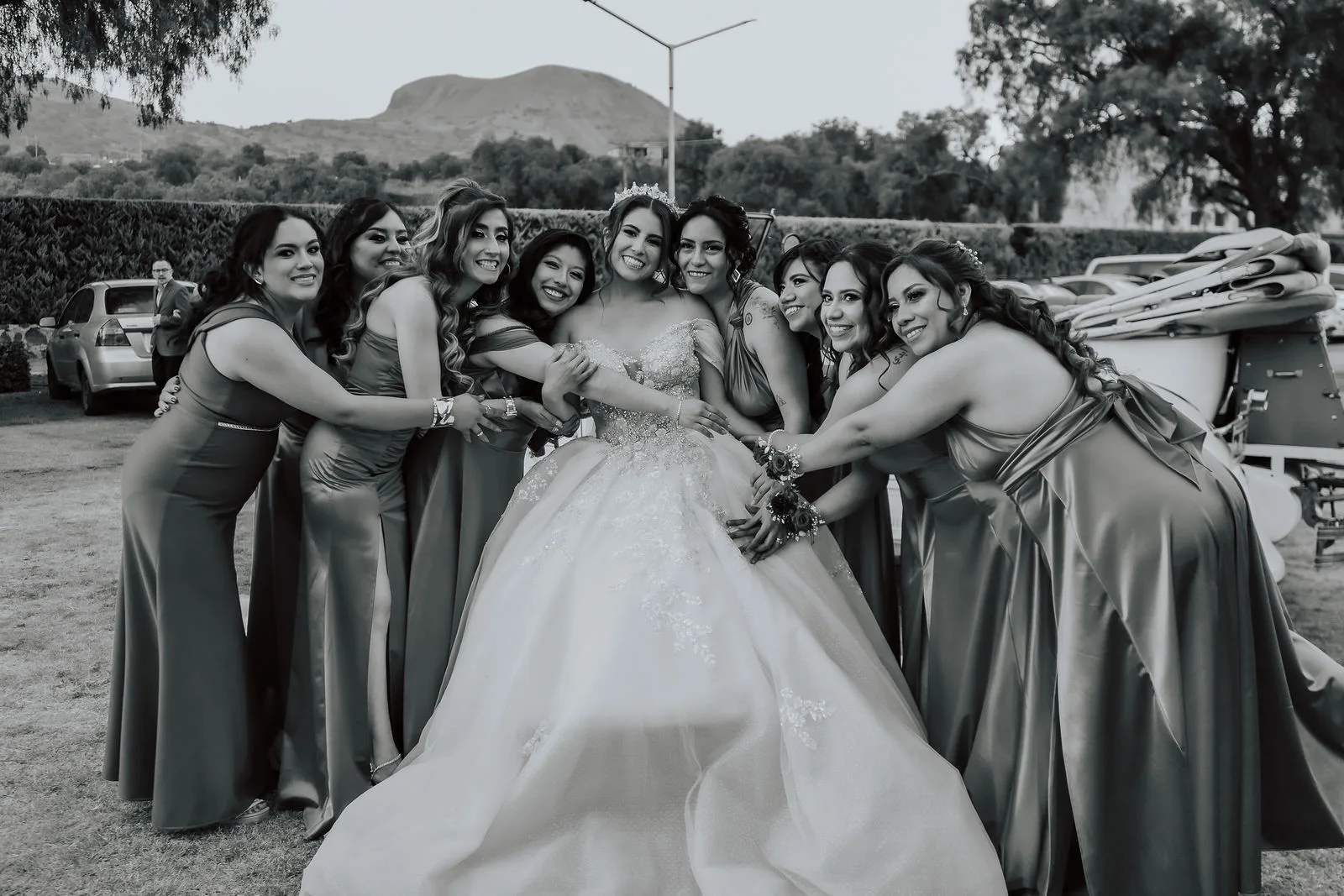 Novia con tiara abrazada por sus damas de honor con vestidos de satín en el jardín de su boda.
